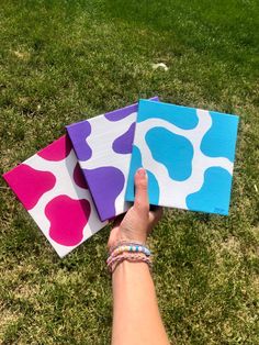 three pieces of paper are sitting on the grass, one is painted like a cow