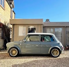 an old grey car parked in front of a house on gravel road next to brick building