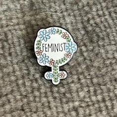 a pin with the word feminist on it sitting on a carpeted surface in front of a gray background