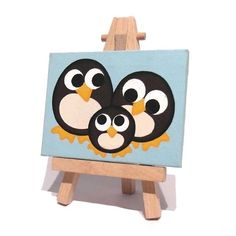 an easel with a painting of three little penguins on it's face and eyes