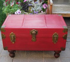 a red suitcase sitting on top of a wooden table in front of a flower garden