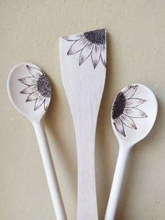 three spoons with sunflower designs on them are sitting next to each other in front of a wall