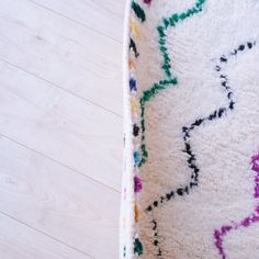 a white rug with multicolored designs on the top and bottom half is laying on a wooden floor