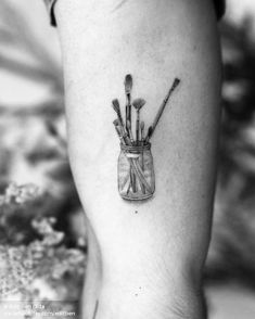 a person with a tattoo on their arm has a jar full of paintbrushes