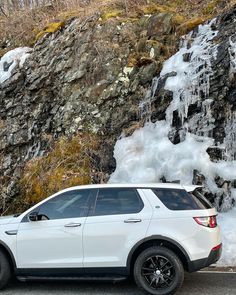 a white suv parked in front of a waterfall with ice on it's sides