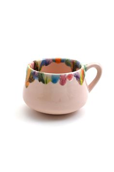 a white cup with colorful flowers painted on the outside and inside, sitting in front of a white background