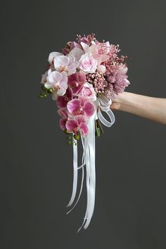 a bridal bouquet with pink flowers and white ribbon tied around the bride's wrist