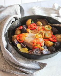 a skillet filled with meat and vegetables on top of a white countertop next to a gray towel