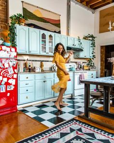 a woman in a yellow dress dancing in a kitchen with blue cabinets and black and white checkered floor