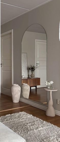 a large mirror sitting on top of a wooden floor next to a white vase filled with flowers