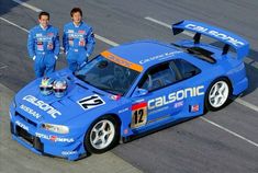 two men standing next to a blue race car