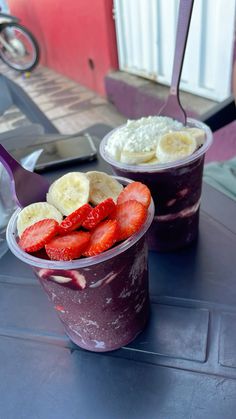 two plastic cups filled with fruit and yogurt on top of a blue table