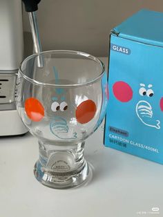 a glass cup with faces painted on it next to a toaster and an unopened box