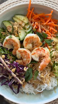 a white bowl filled with shrimp and veggies next to carrots on top of noodles