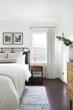 a bedroom with white walls and wood flooring, two framed pictures on the wall