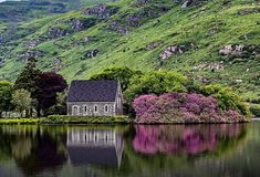 a house sitting on top of a lush green hillside next to a lake filled with water