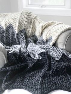 a gray and white knitted blanket sitting on top of a couch next to a window