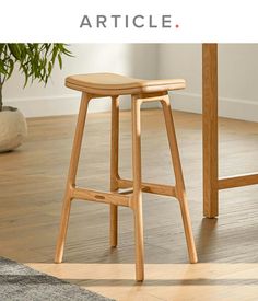 a wooden stool sitting on top of a hard wood floor next to a potted plant