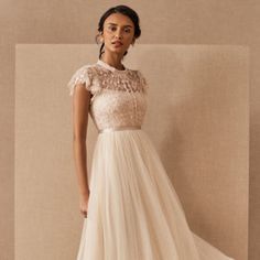 a woman in a white dress standing next to a beige wall and looking at the camera