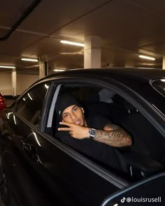 a man sitting in the driver's seat of a car with his hand up