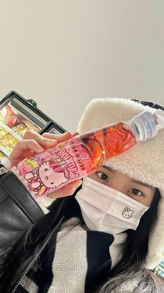 a woman wearing a hello kitty mask and holding up a plastic bottle with an orange liquid in it