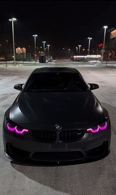 a black car parked in the middle of a parking lot at night with its lights on