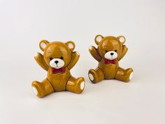 two brown teddy bears sitting next to each other on a white surface with one holding the other's hand