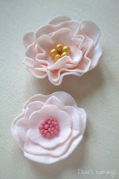 two pink flowers with gold centers sitting on a white tablecloth, one in the shape of a flower