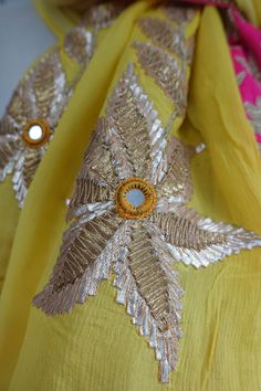 an embroidered yellow scarf with gold and silver leaves on it's side, along with a button in the center