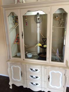 a white china cabinet with glass doors and drawers on the bottom, in front of a wall