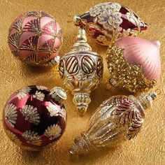 several ornaments are sitting on a gold surface, one is red and the other is pink