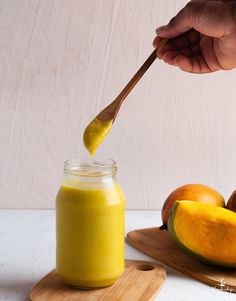 a person holding a spoon over a jar filled with mango butter next to peaches