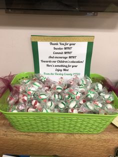 a green basket filled with candy on top of a wooden table next to a sign