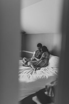 a man and woman sitting on top of a bed next to each other in black and white