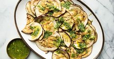 a white plate topped with eggplant covered in pesto next to a green sauce