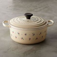 a white casserole with floral designs on it and the words le creuset written in french