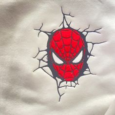 a spiderman face is seen through the holes in a white t - shirt that has been embroidered onto it