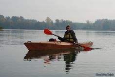 a man in a kayak paddling on the water with trees in the background