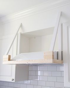 a kitchen with white tile and wooden shelves above the stove top, under construction work