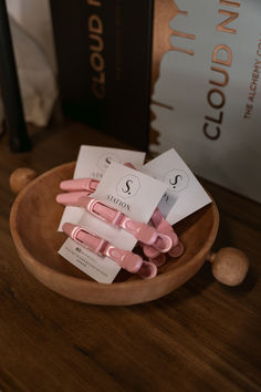 pink and white clips are in a wooden bowl on a table next to some books