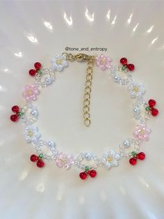 a white bracelet with red and pink beads, pearls and cherries on a gold plated chain