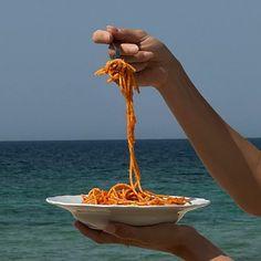 a person is holding a bowl of food over the ocean and reaching out to eat it