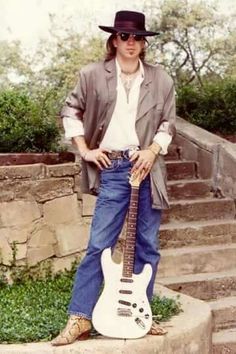 a man with a hat and sunglasses standing next to a white guitar on some steps