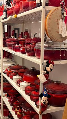 many red pots and pans are stacked on shelves in a store with mickey mouse figurines