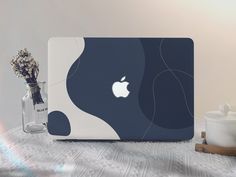 an apple laptop sitting on top of a table next to a vase with dried flowers