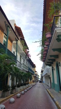 an empty street lined with tall buildings and potted plants on the side of it