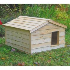 a wooden dog house in the grass with a red bird sitting on it's side