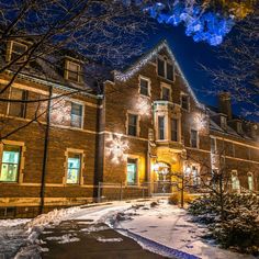 a large brick building with christmas lights on it's windows and trees in the snow