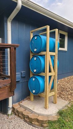 three blue barrels are stacked up on a wooden rack in front of a blue house