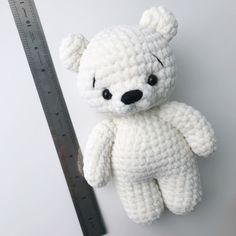 a white crocheted teddy bear next to a ruler